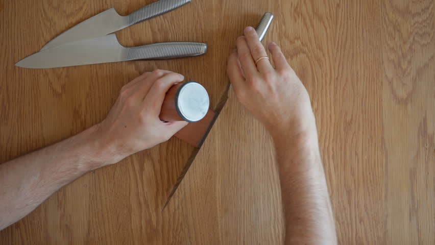 Demonstration of knife sharpening, using a rolling knife sharpener to hone a blade. A man shows the workflow, flipping the knife on its magnetic holder to sharpen both sides. Includes original audio