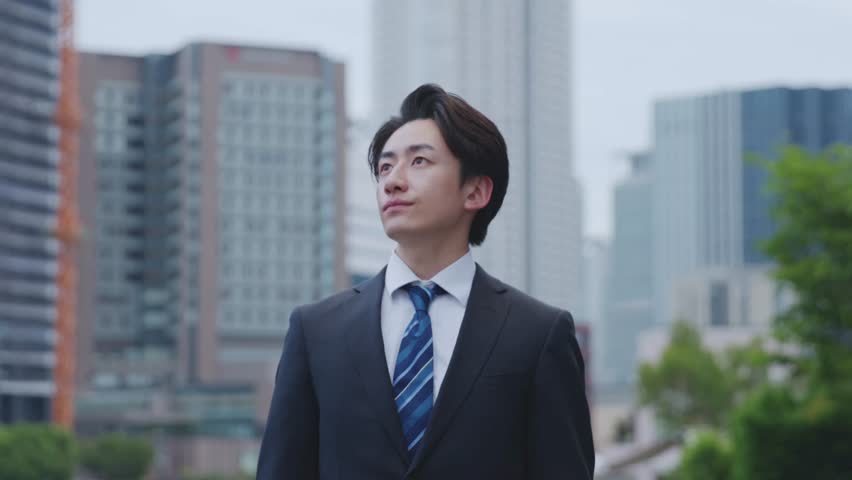 A Japanese businessman in a suit gazing into the distance with a building in the background