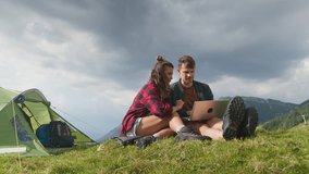 Happy campers couple enjoying a relaxing getaway, connecting with nature and having fun via laptop, mixing technology and outdoor adventure, handheld shot. - Powered by Shutterstock - Get 15% off with code: PIKWIZARD15