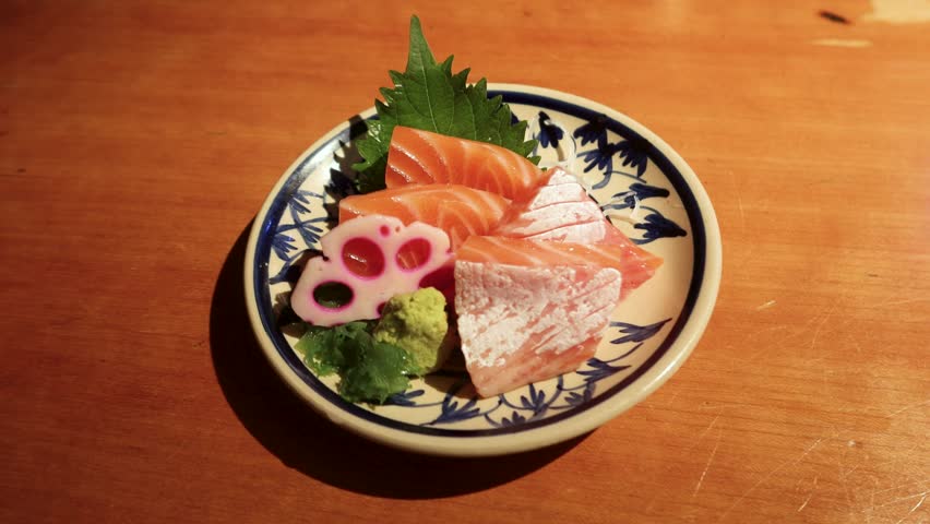 closse up of four slices of raw fresh salmon tummy sashimi with wasabi on the side on a Japanese pattern plate on a wooden table with copy space