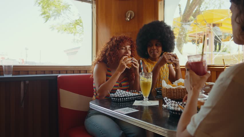 Multiethnic group of friends having meal at 80s vintage diner restaurant - Multicolored young people bonding and having fun, eating in an american fast food burger house	