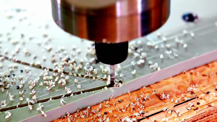 CNC router cuts into material while tiny flake particles fly from blade in detailed view