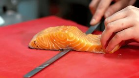 A close-up shot shows a professional chef's hands skillfully using a long filleting knife to slice the skin away from a fresh, raw salmon fillet on a red cutting board. - Powered by Shutterstock - Get 15% off with code: PIKWIZARD15