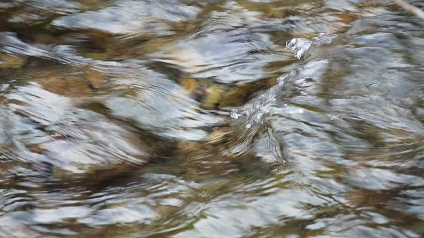 Close-up video of the surface of a cold mountain river with clear clear cold water, on which waves arise due to the collision of a stream with underwater rocks, in real time video with sound, 100 fps