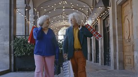 Elegant senior couple enjoying a shopping spree, walking together under festive string lights, carrying colorful shopping bags and sharing laughter - Powered by Shutterstock - Get 15% off with code: PIKWIZARD15