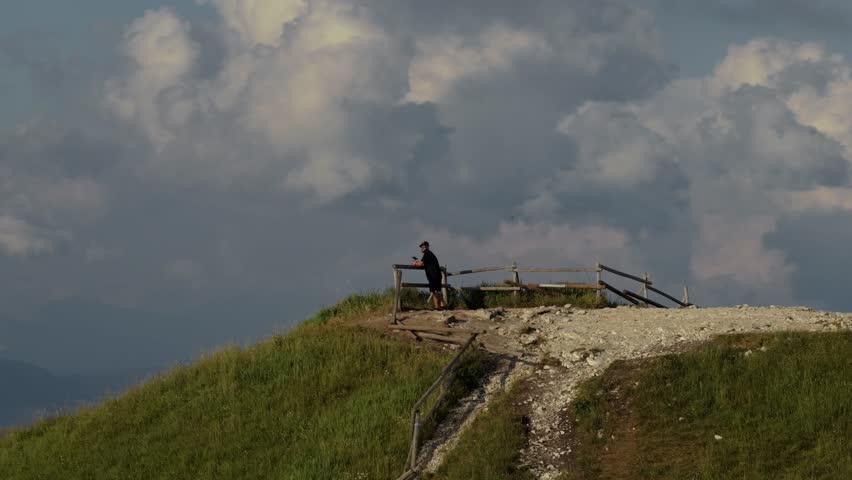 Fast orbital drone shot of man standing on mountain peak with dynamic parallax clouds