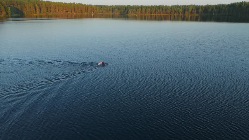 A man in a wetsuit is swimming across a forest lake. It is a marathon swimming competition. Open water swimming.