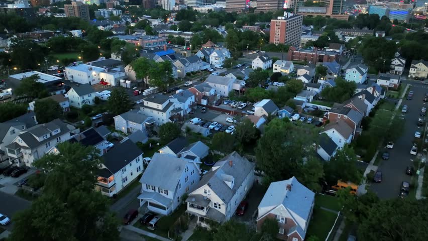 Residential area with homes and apartments in Stamford city, Connecticut. Night scene with lighting skyscrapers of downtown in background. Aerial tilt up wide shot.