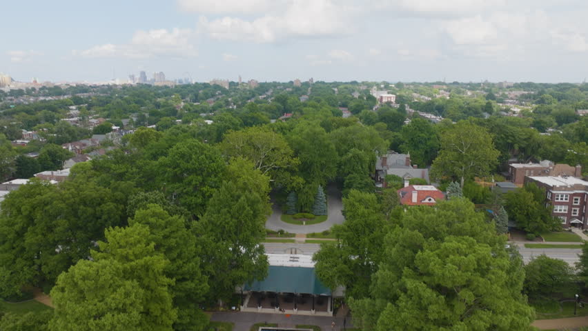 Cinematic aerial tilt down over Tower Grove neighborhood homes in St. Louis, Missouri on a bright summer day, revealing tree-lined streets and residential architecture.