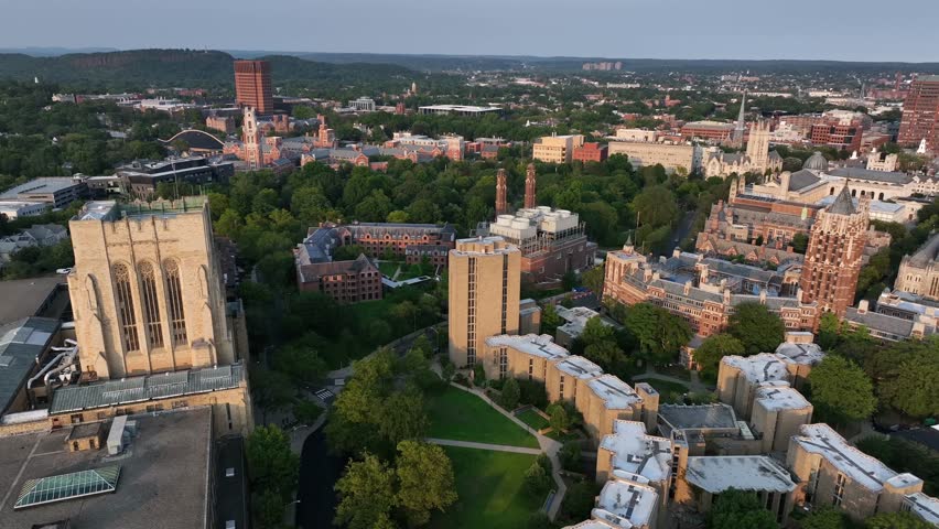 Aerial view of New Haven, Connecticut, showing Yale University’s historic campus with Gothic architecture, green spaces and surrounding urban skyline. Sunset time in summer. Wide shot.