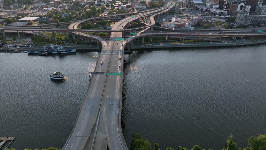 Boat on Hudson River in the morning. Skyline with modern towers and skyscrapers or downtown Albany, New York. Drone tilt up wide shot. Traffic on elevated highways.