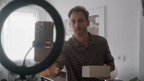 Man recording vlog or social media reel reviewing product unboxing video live stream. UGC style influencer talking to mobile phone in home studio. Excited and happy content creator opening white box - Powered by Shutterstock - Get 15% off with code: PIKWIZARD15