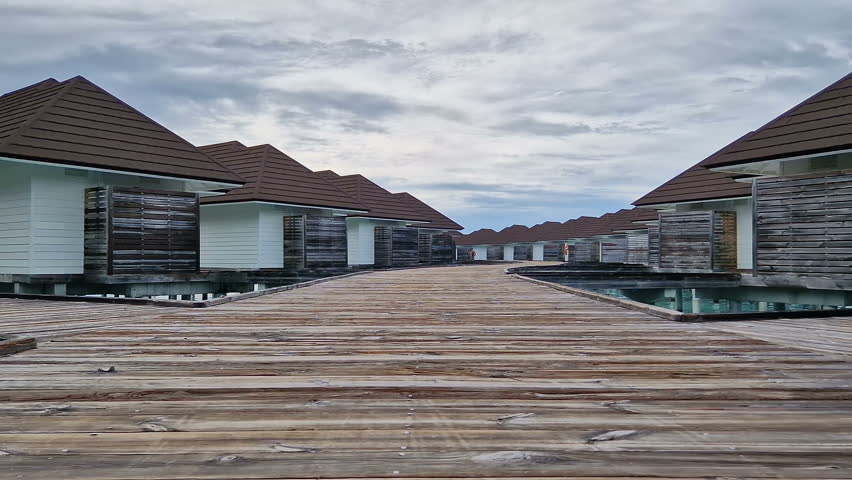 Maldives. A young woman in a blue shirt walks across the bridge. A romantic honeymoon.