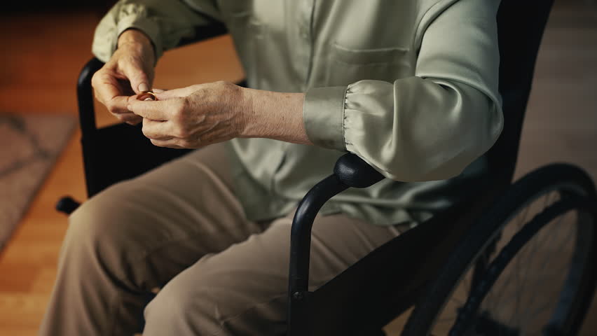 Senior widow in wheelchair holding wedding ring, mourning loss and memories