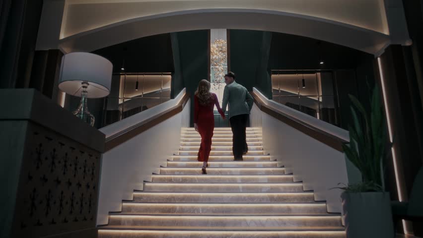 Climbing the stairs together holding hands inside an interior with luxurious fittings