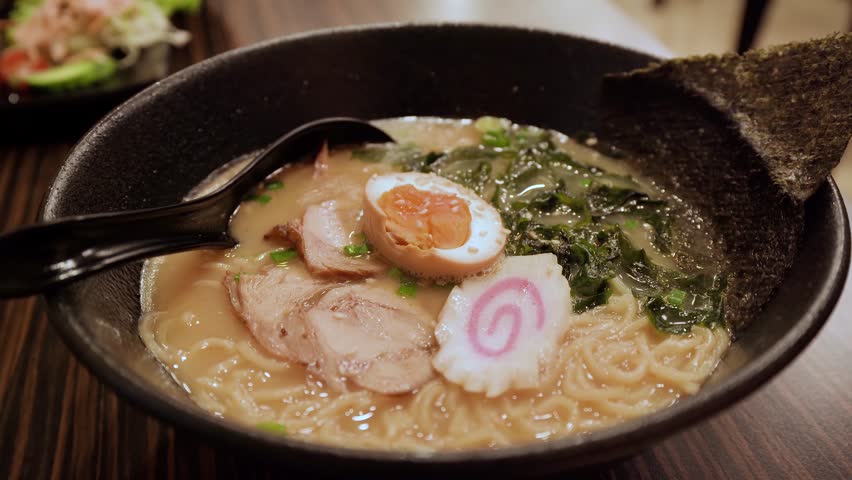 Japanese ramen presented in a rich broth, topped with soft-boiled egg, seaweed, and pork.