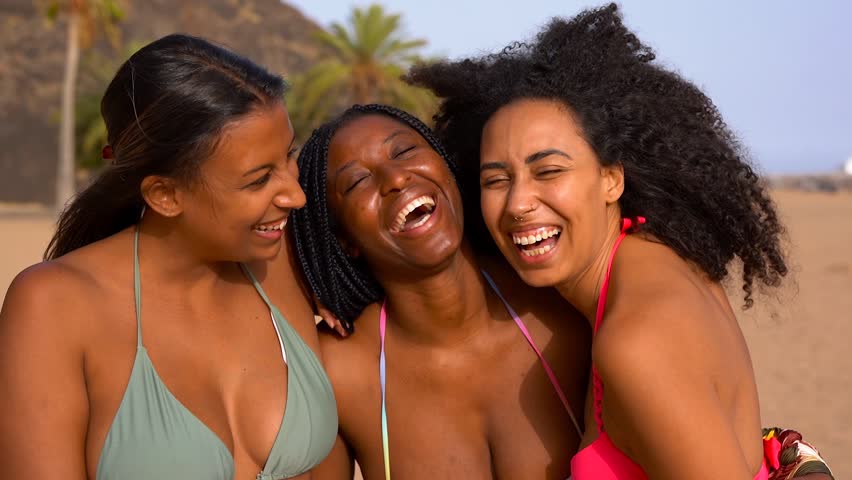 Group of multiracial women hugging each other on the beach during summer vacation wearing colorful bikini - Diverse female friendship, holiday and young people concept 