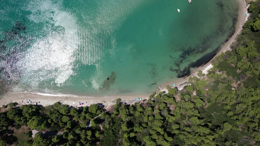 Sunlight illuminates the crystal-clear turquoise water as gentle waves caress the sandy beach, creating a mesmerizing dance of light and shadow along the shoreline. Chalkidiki greece