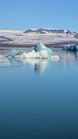 Jokulsarlon Glacier Lagoon showcases stunning icebergs glistening under the Icelandic sun, surrounded by majestic mountains. The serene waters create a mesmerizing reflection of natures beauty.