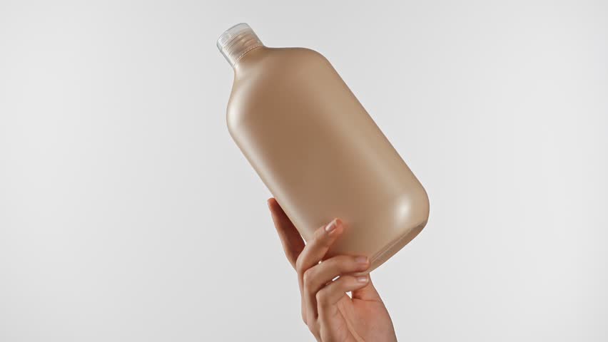Hand holding a beige plastic bottle, likely for shampoo or conditioner, set against a simple white background.