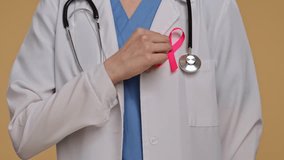 Doctor in white coat with stethoscope and pink ribbon on neutral background, points finger at ribbon as a symbol of awareness. The concept of breast cancer awareness day. - Powered by Shutterstock - Get 15% off with code: PIKWIZARD15