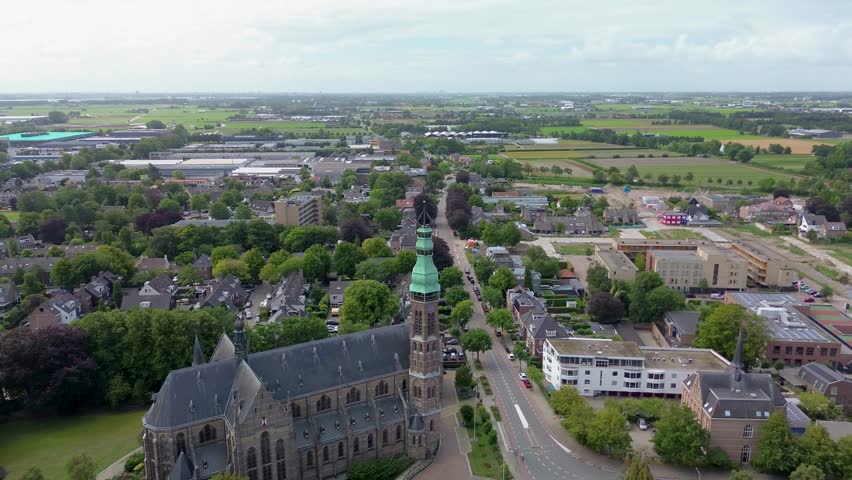 A stunning aerial view of a European town with a historic church and green fields stretching to the horizon. The mix of architecture, roads, and nature creates a peaceful and picturesque scene.