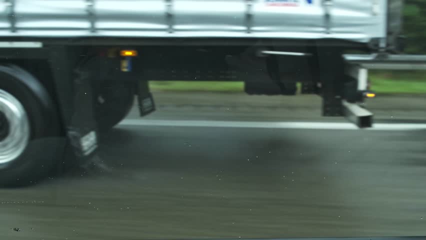 Close-up of the wheels of a truck driving on a motorway on wet asphalt in heavy rain. The danger of the gliding effect on a wet road. Concept of speed limits during bad weather.
