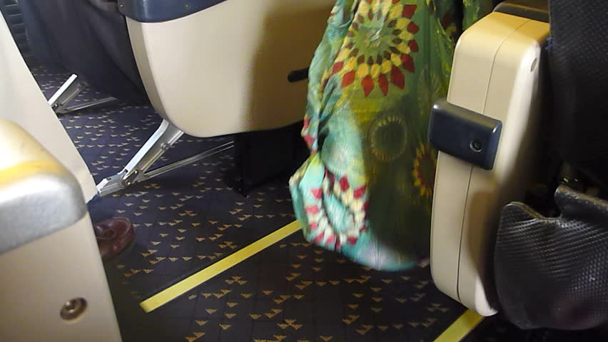 Interior airplane as passengers walk by with bags and luggage.