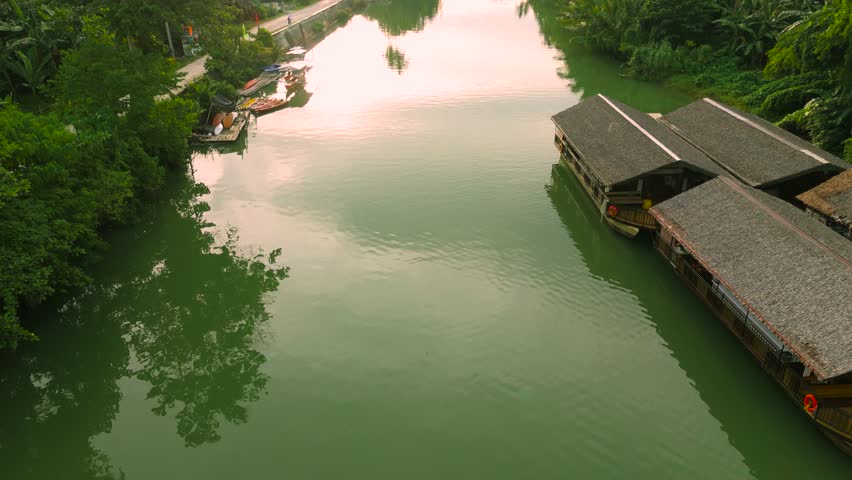 Aerial view of a narrow Amazon River channel with thatched structures, boats, and people on the riverbank, amidst tropical vegetation.