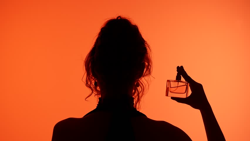 A silhouette of a woman holding a perfume bottle against a vibrant orange background, evoking elegance and mystery.