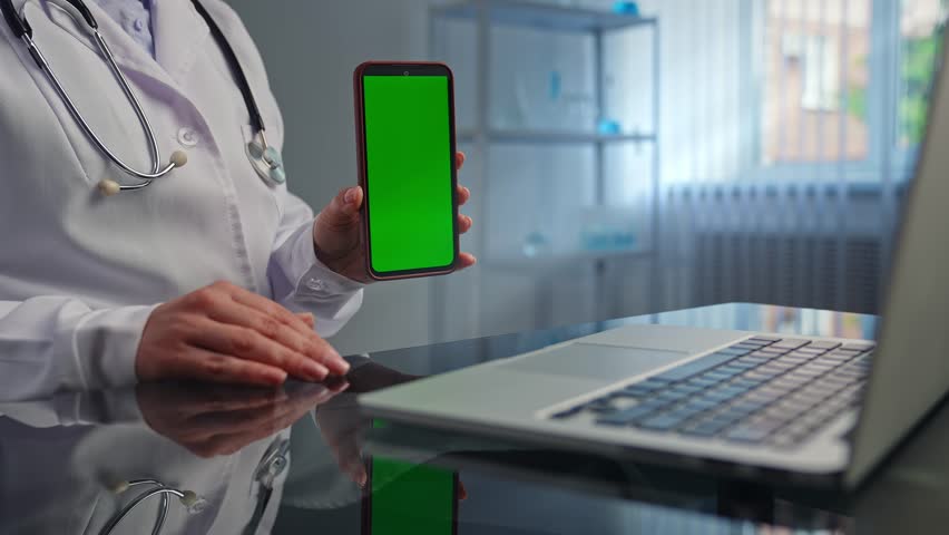 A doctor in a clinic showcasing a smartphone with a green screen, indicating technology integration in healthcare. Advertising area, workspace mock up