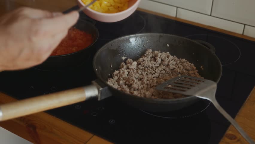 Man pours chopped yellow bell pepper from bowl into cast iron skillet with fried minced meat on stove. Cooking healthy homemade meal with fresh vegetables. High quality 4k footage