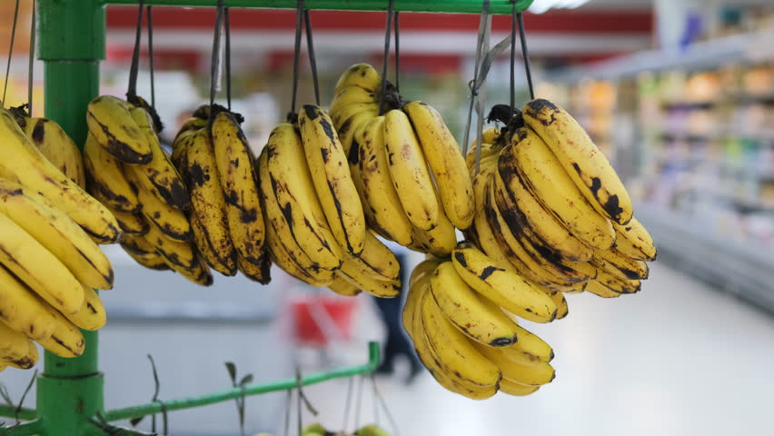 A woman selects ripe bananas from a display in a grocery store. She values natural and vegan foods, showcasing her healthy lifestyle choice. Fresh organic produce