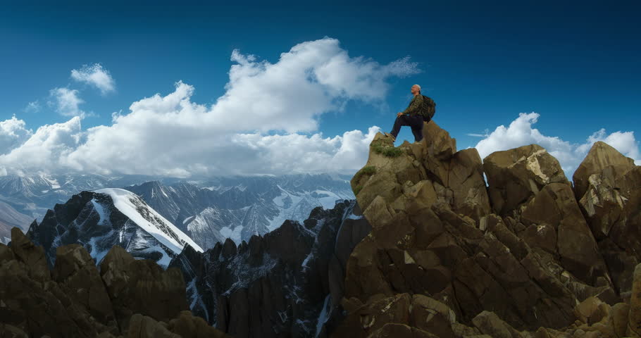 Man with a backpack conquering a peak against the backdrop of mountains.