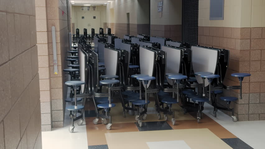 Row of foldable cafeteria tables with attached round stools, stored in a hallway or storage area of a school or institutional building.