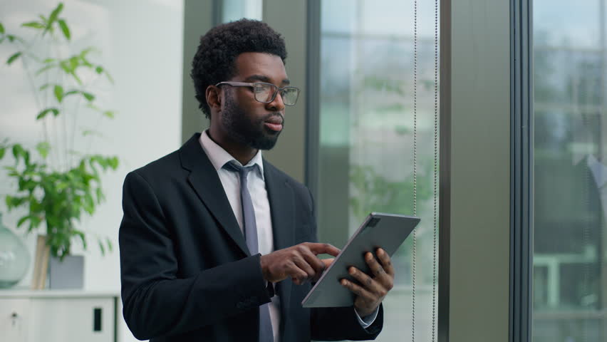 Thoughtful African American businessman in office concentrate using digital tablet looking out window focused business male man guy using technology device thinking planning strategy professional work - Powered by Shutterstock - Get 15% off with code: PIKWIZARD15
