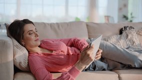 Calm woman reading ebook lying on cozy apartment couch at domestic morning closeup. Relaxed brunette watching tablet resting on home sofa. Smiling lady browse email at tab computer in modern interior. - Powered by Shutterstock - Get 15% off with code: PIKWIZARD15