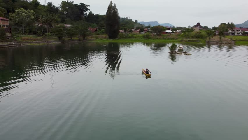 Drone orbit left to right with altitude gain around fisherman in canoe on Lake Toba, Sumatra. Aerial reveal of village, palm trees, and lake. Ideal for travel, cultural and cinematic projects.