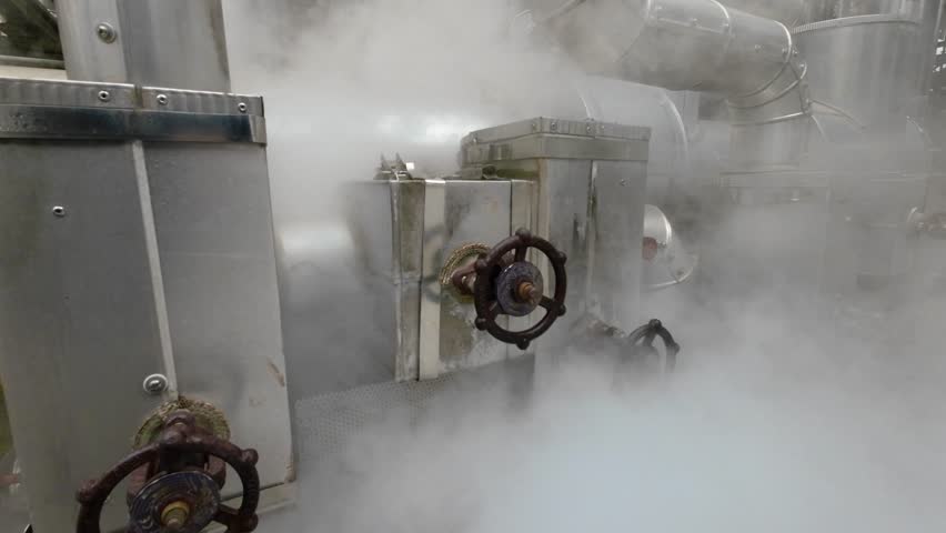 Industrial interior. Close-up of a lot of pipes, pressure gauge and a shut-off valves on the pipes in open air chemical plant. Jets of hot steam from valve. Production of thermal energy and hot water