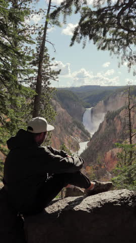 Tourist sitting with stunning and breathtaking view of the magnificent Lower Falls in Yellowstone National Park, capturing incredible and unparalleled beauty of nature in beautiful state of Wyoming