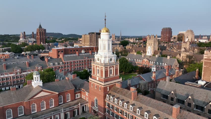 Aerial flight over Davenport college with courtyard and church tower with golden cupola. Passing by shot. Harness. Tower of Yale university in background. New Haven, Connecticut at sunset.