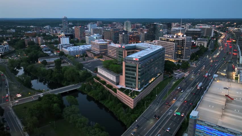 Stamford , United States - 08 03 2025: Busy roads of Stamford, Connecticut at dusk. Mill River and illuminated downtown buildings. Aerial rising wide shot. UBS buildings and skyline.