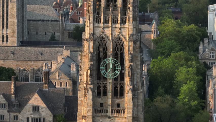 Harkness tower in Collegiate Gothic architecture on campus of Yale university. Sunset time in New Haven, Connecticut. Aerial zoom shot. Historic houses and homes in background.