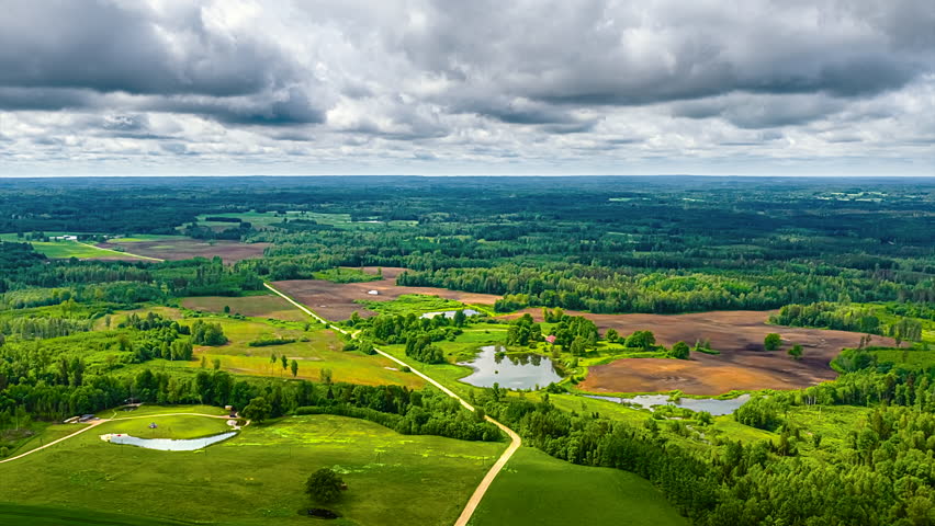 Forested fields and hills with fast-moving clouds creating shadows over rural, panoramic high angle