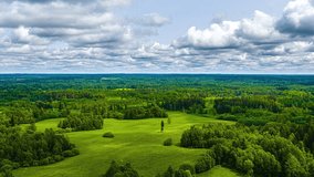 A captivating time-lapse shows dynamic clouds moving across a blue sky, casting shadows over a vast, green Latvian landscape of dense forests interspersed with bright, open grassy clearings. - Powered by Shutterstock - Get 15% off with code: PIKWIZARD15