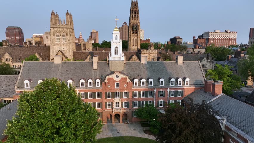 Aerial flyover Yale University campus in New Haven, Connecticut, with Georgian-style dormitory, Gothic spires and the city skyline under clear summer sky. Wide shot. Small American city.