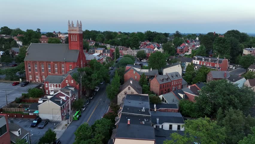 Aerial flyover historic town with ancient buildings and old church in Lancaster, Pennsylvania. Dusk scene in summer season. Brick houses on small cozy town.