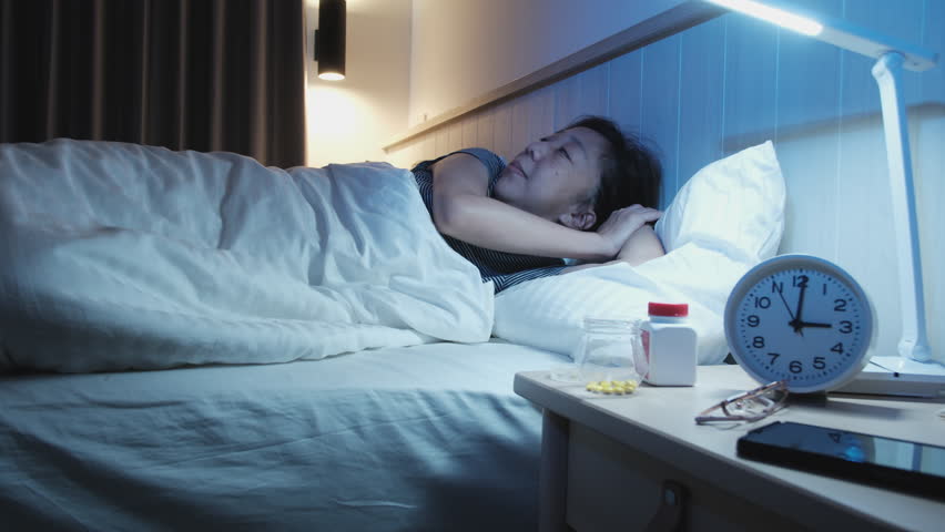 Female Asian middle-aged person has a sleep disorder, is stressed, and worries awake at night from drug side effects, insomnia illness in bedroom, mature and menopausal woman's healthcare problem.