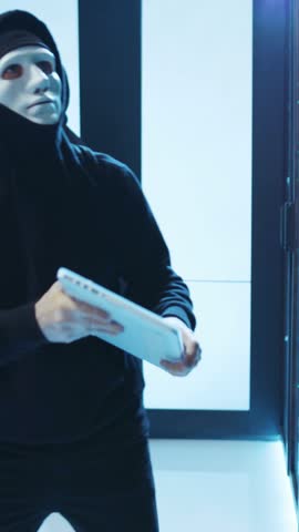 A mysterious figure wearing a mask stands with a tablet in an advanced hightech environment