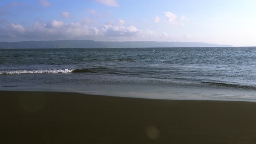 waves crashing on Black Sand beach,
Seascape against clear blue sky with rocky island